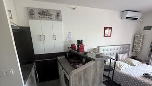 A compact hotel room with a kitchenette, a bed with striped bedding, and a small seating area.