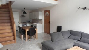 Ein moderner Wohnraum mit Treppe, einem Essbereich inklusive Holztisch und Stühlen, einem grauen Sofa und einer Küche mit weißen Schränken und einer Mikrowelle.