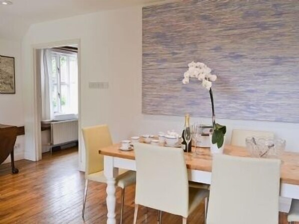 A dining area with a wooden table, white chairs, and a large abstract painting on the wall.