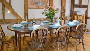 Ein Esszimmer mit einem Holztisch, gedeckt für sechs Personen, umgeben von sechs Stühlen. Darüber an der Wand hängt ein Gemälde.