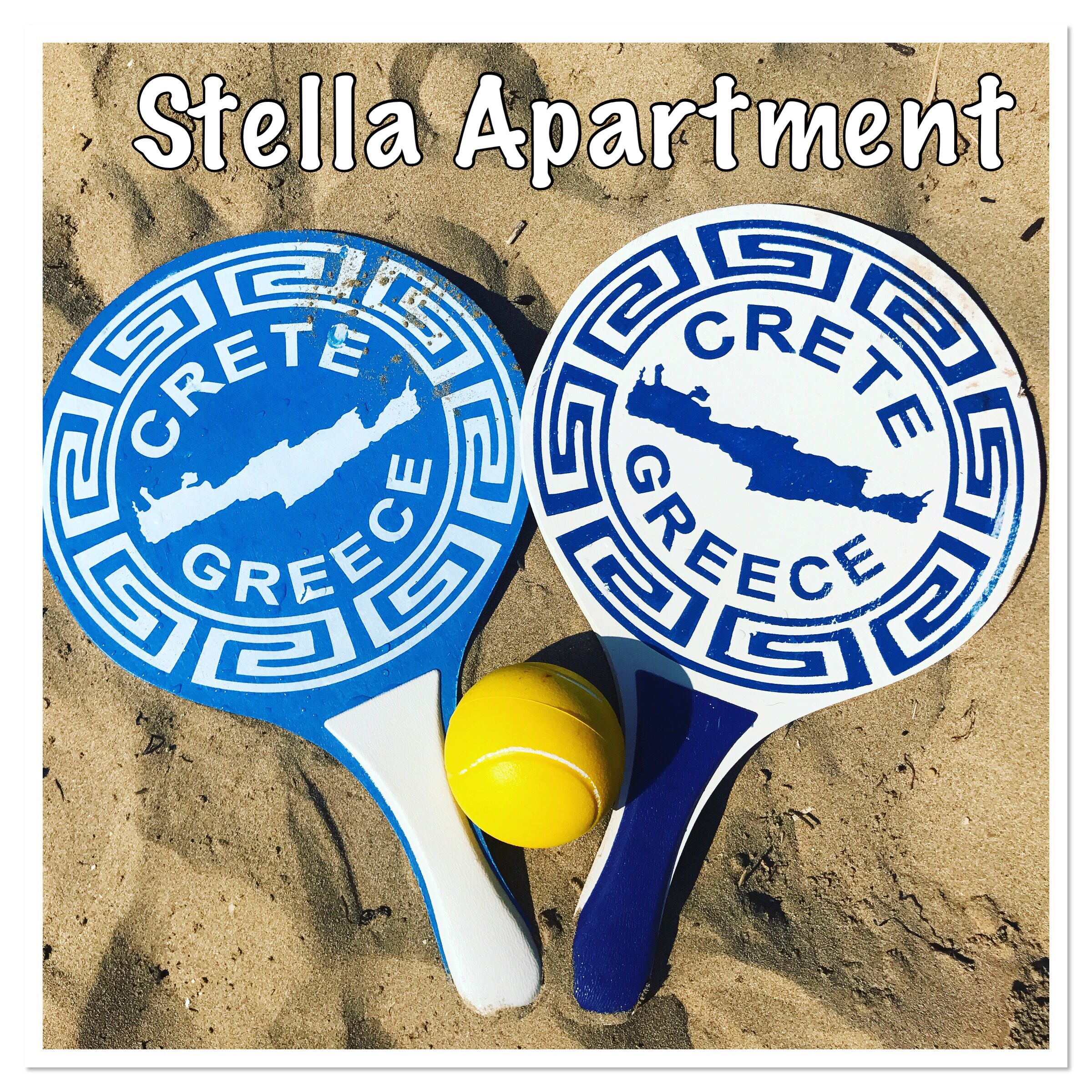 Two blue and white Crete Greece paddleboards with a yellow ball on a sandy surface.