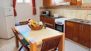 A kitchen with wooden cabinets, a white refrigerator, a microwave, an oven, a dining table with chairs, and a window with curtains. - ☀️Stella Apartment☀️Almyrida 350m from the Sea, you don't rent a Car (Almyrida)