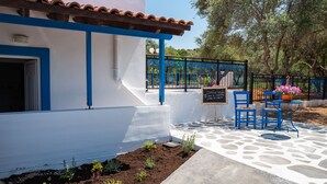 A building with a white exterior and blue trim, a stone-paved patio, and a black metal fence with a sign. - ☀️Stella Apartment☀️Almyrida 350m from the Sea, you don't rent a Car (Almyrida)