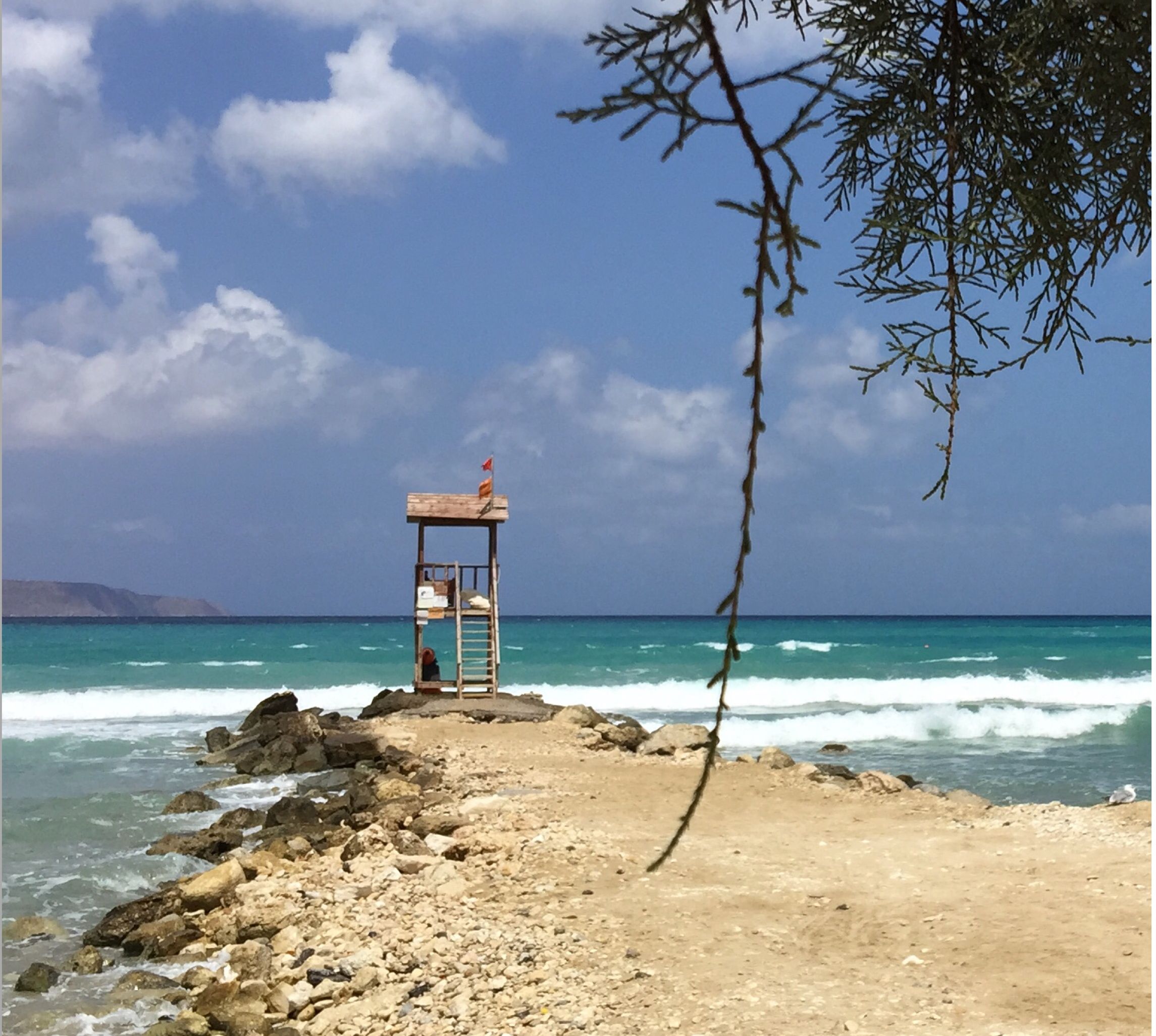 A beach with a lifeguard tower, rocky shoreline, and clear blue sea.