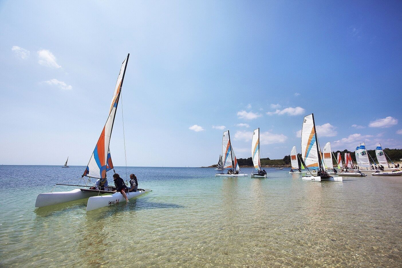 A calm coastal area with several sailboats anchored near the shore.