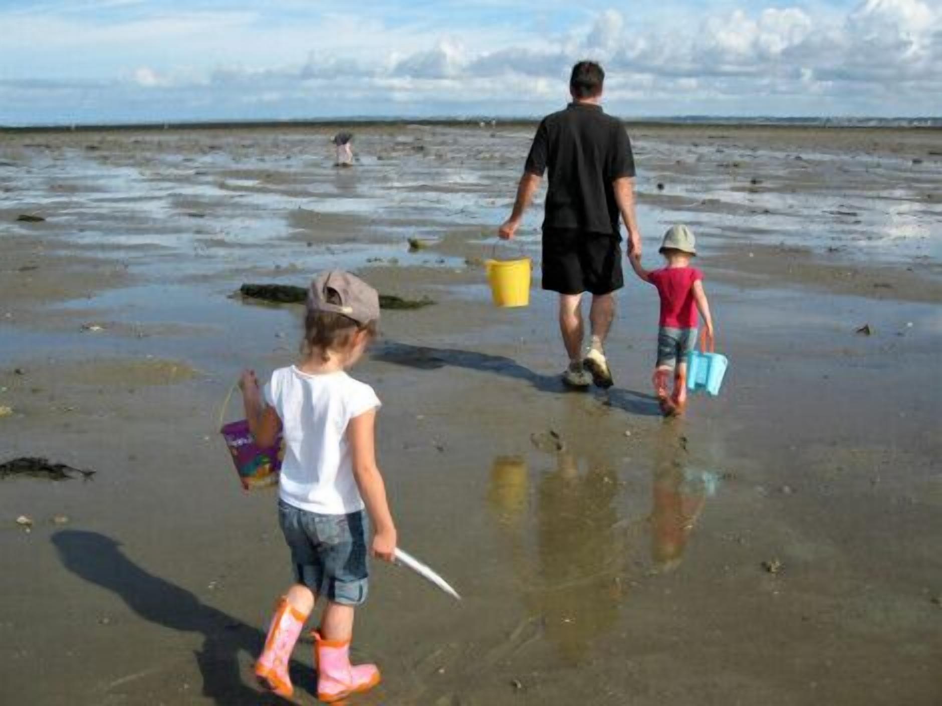 Een zandstrand met mensen die lopen en spullen vasthouden zoals emmers en speelgoed.