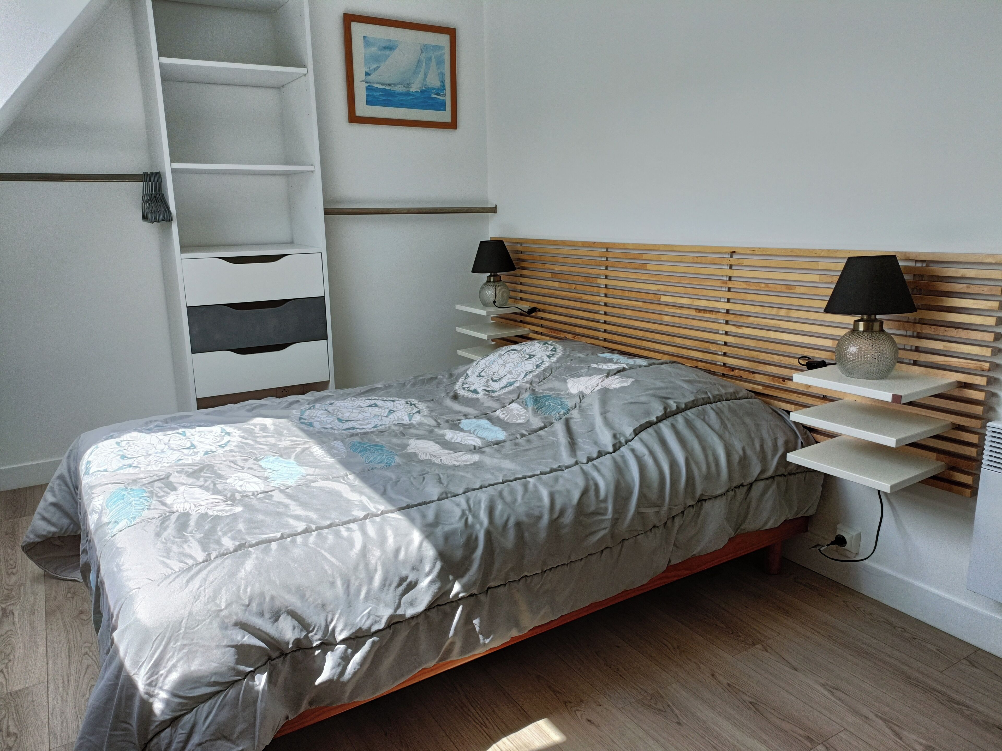 Een slaapkamer met een bed, nachtkastje, lamp, plank en een schilderij aan de muur.