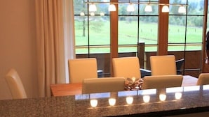 Una camera d'albergo con un piano di lavoro in granito, un tavolo da pranzo con sedie, un'ampia finestra con vista su un paesaggio verde e un lampadario.
