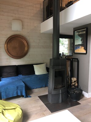 Un salon chaleureux avec un canapé, un grand miroir rond, une cheminée et une affiche accrochée au mur.