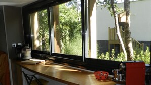 Eine Küche mit einem großen Fenster, Holzschränken, einer roten Kaffeemaschine und zwei gelben Stühlen.