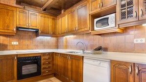 Een keuken met houten kastjes, een inbouwoven, een vaatwasser en een magnetron.