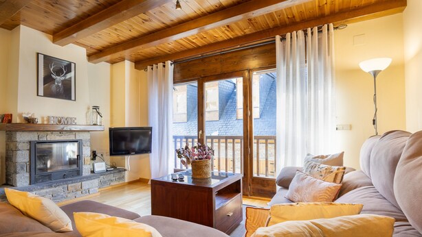 Een gezellige woonkamer met een open haard, comfortabele zithoek en een groot raam met gordijnen.