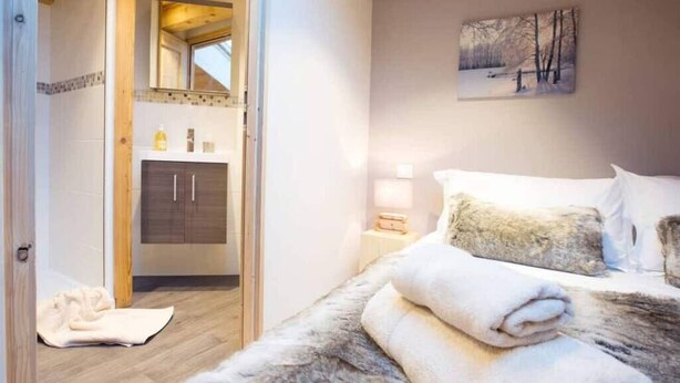A bedroom with a large bed, a fluffy rug, a wooden floor, a bathroom with a mirror, and a painting on the wall. - Apartment la Ranche, Montriond (Montriond)