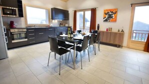 A modern kitchen with dark cabinetry, a dining table set for four, and a large window with curtains. - Apartment la Ranche, Montriond (Montriond)