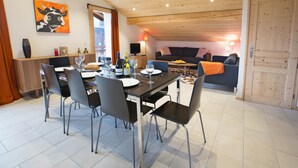 A dining area with a wooden table set for four, surrounded by chairs. A sofa and a television are visible in the background. - Apartment la Ranche, Montriond (Montriond)