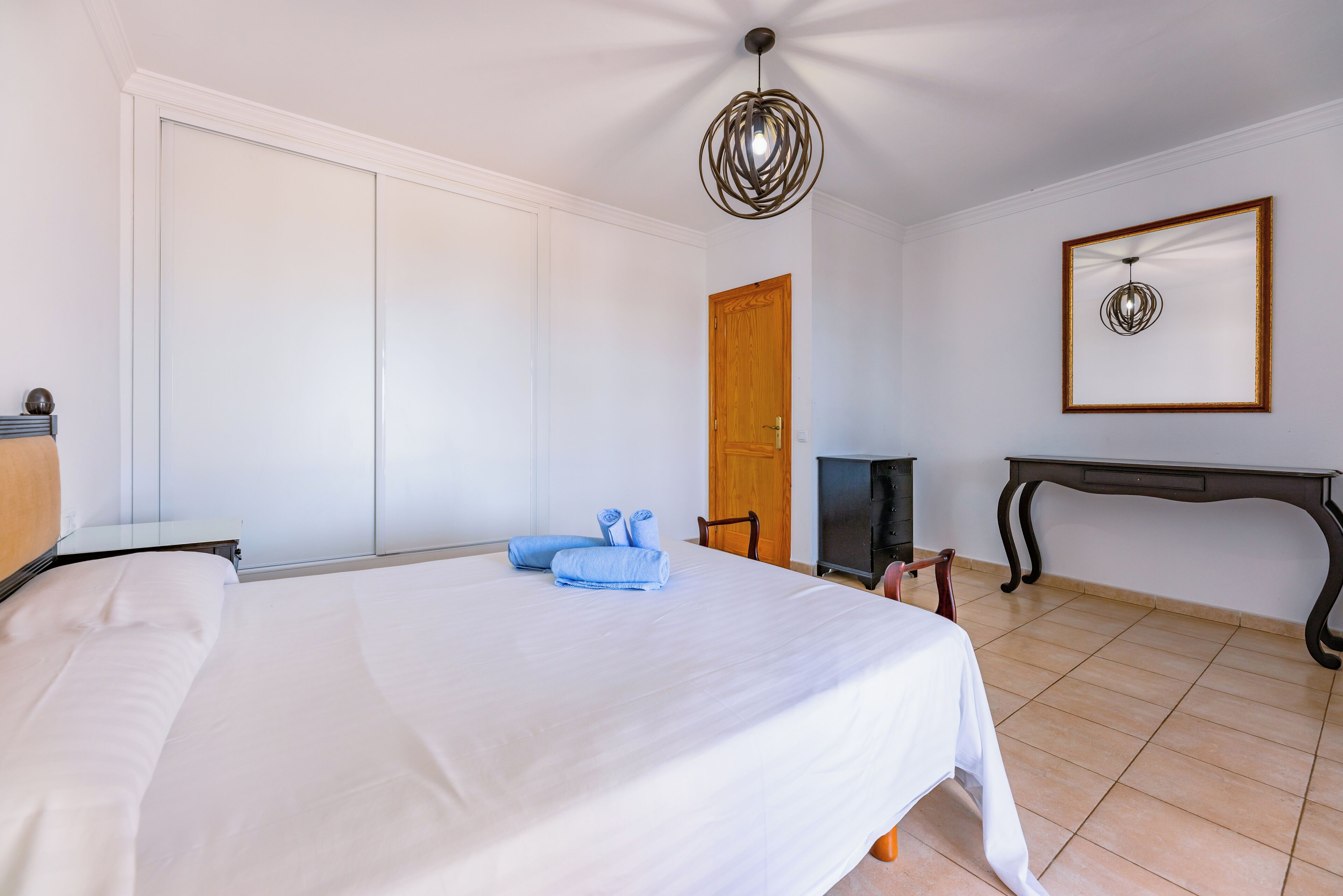 A bedroom with a bed, a wooden door, a mirror, and a small table.