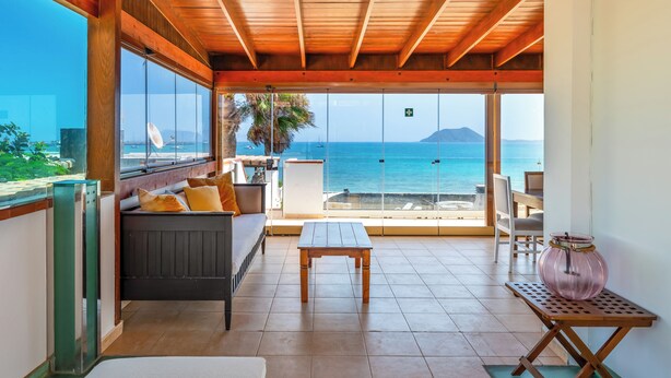 A spacious balcony with a wooden ceiling, a sofa with cushions, a small table, and a glass door leading to the sea. - Private, independent villa on the first line, terrace and tranquility
 (La oliva)
