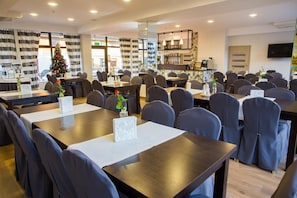 A dining area with multiple tables and chairs, a Christmas tree, and a bar area with shelves of bottles.