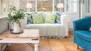 Una habitación con un sofá blanco, un sillón azul, una mesa de madera y un jarrón con flores.