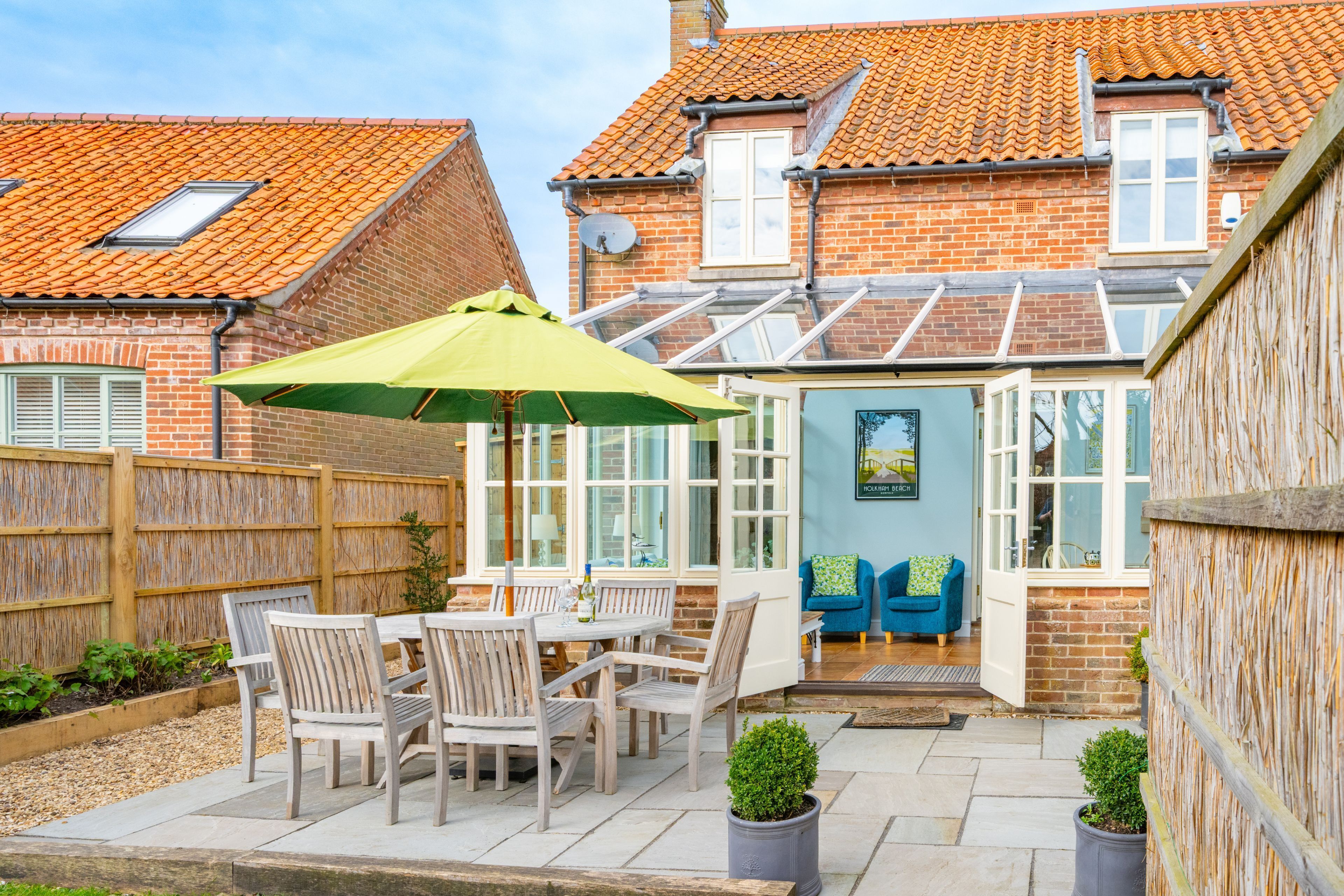 A patio with a table and chairs, a green umbrella, and a brick house with a tiled roof.