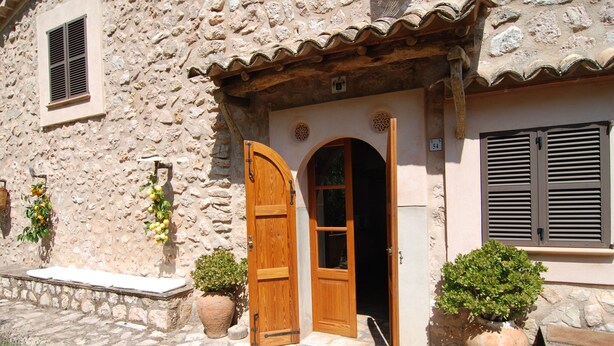 Un edificio in pietra con una porta e persiane di legno, una piccola finestra e piante in vaso.