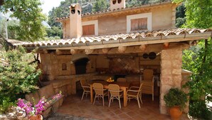 Una terrazza all'aperto con pavimento in pietra, un tavolo e sedie, e una pianta in vaso.