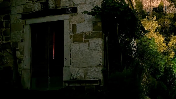 Un bâtiment en pierre avec une fenêtre éclairée et une enseigne indiquant « 5b ».