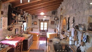 Un intérieur rustique en pierre, avec des poutres en bois, un coin repas et une cuisine aux murs de pierre, équipée de divers ustensiles.
