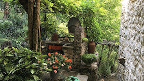 Un mur de pierres bordant un espace cuisine extérieur de style rustique, comprenant une cheminée en pierre, des ustensiles de cuisine et un porte-ustensiles suspendu.