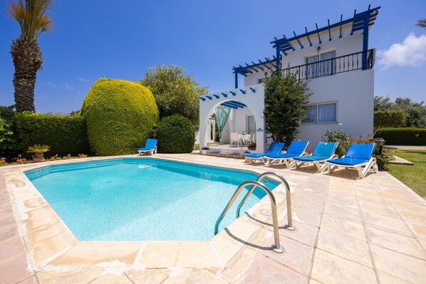En swimmingpool med liggestole, en pergola og en hvid bygning med balkon.