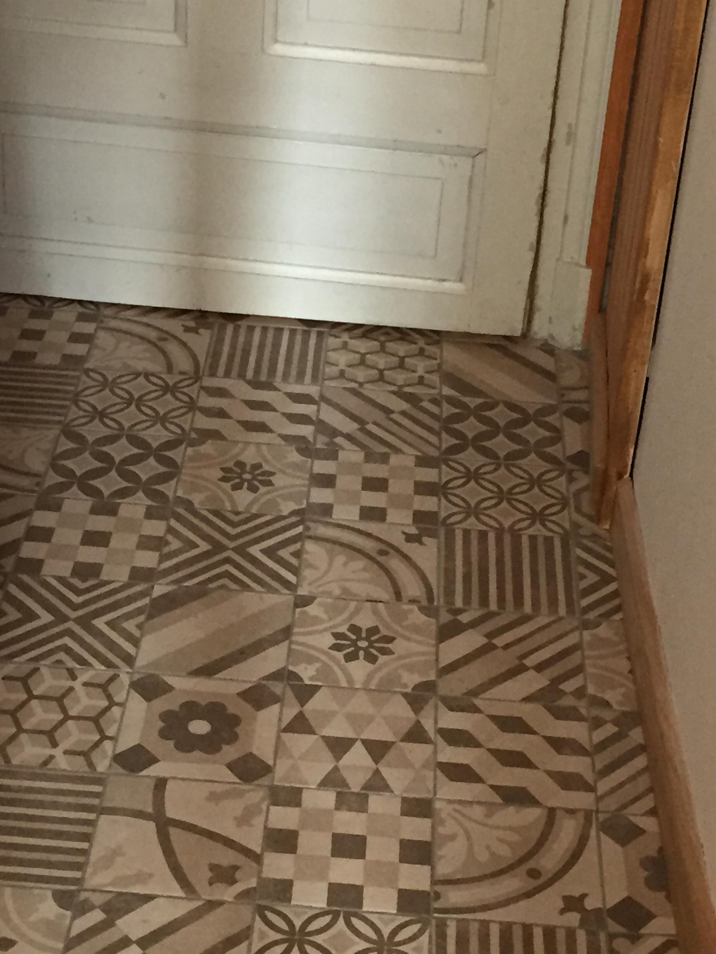 Un passadís amb rajoles estampades que condueix a una porta blanca.