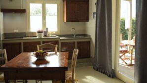 Una cocina con una mesa de madera, sillas, un frutero, un lavamanos y armarios.