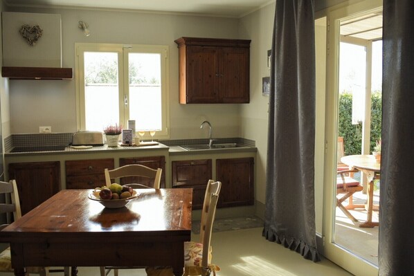 A kitchen with a wooden table, chairs, a fruit bowl, a sink, and cabinets.