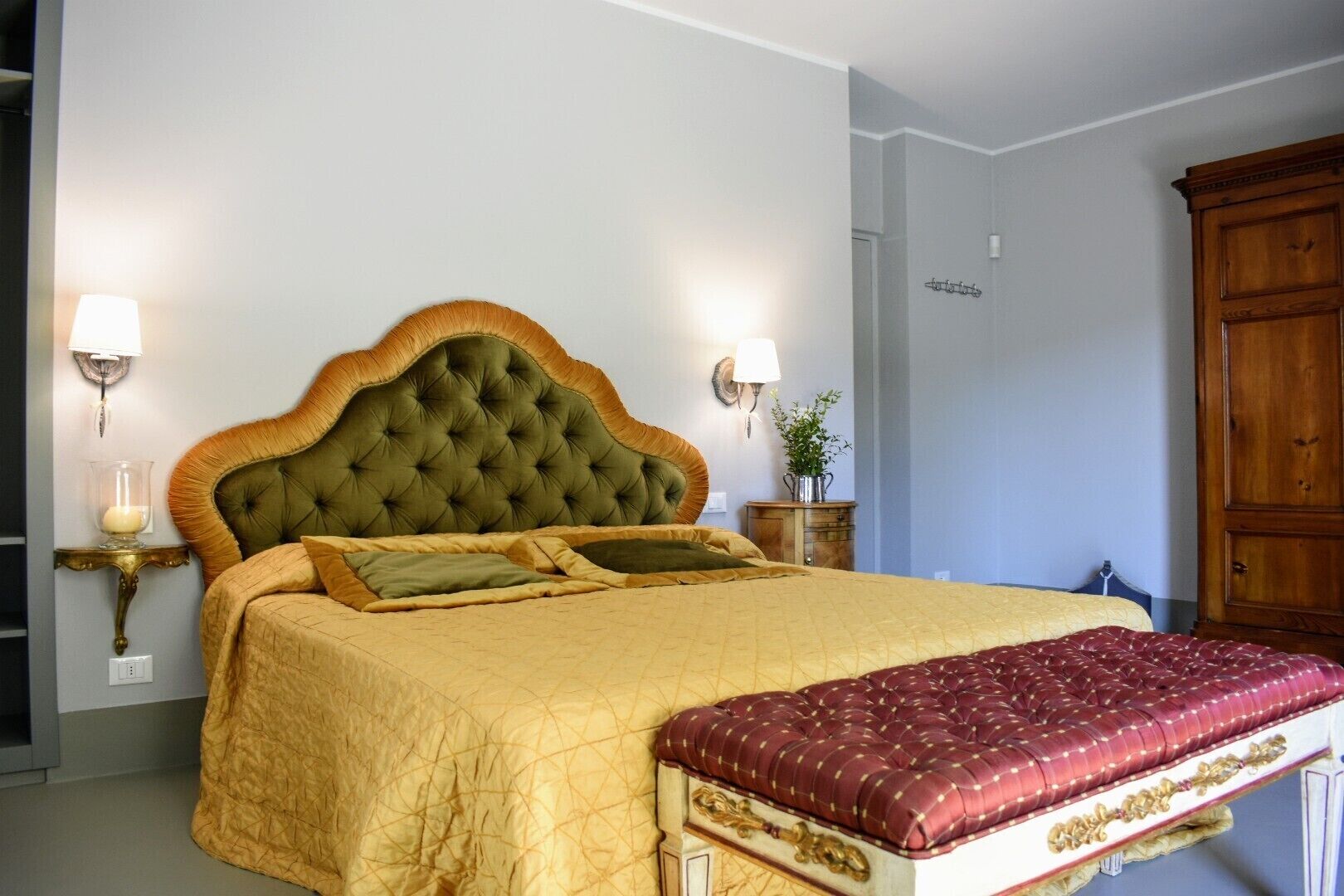 Un dormitorio con una cama grande, dos lámparas de noche, un armario de madera y una mesita con una planta.