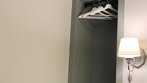 Un armario alto y estrecho con varios estantes y una barra para colgar ropa, una lámpara de pared y una pequeña mesa con una vela.