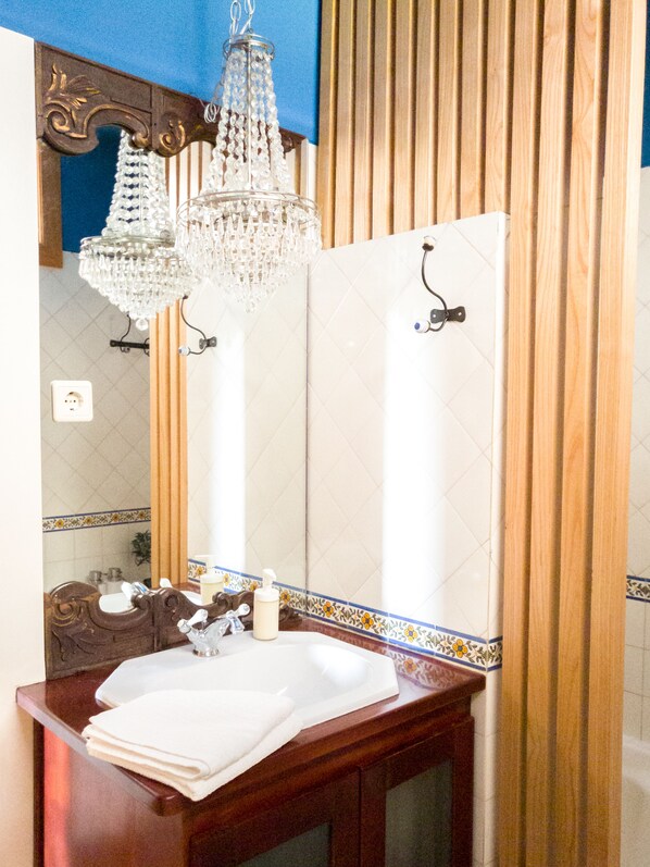 A bathroom with a wooden vanity, a white sink, a mirror, and a chandelier.