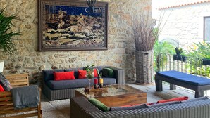 Un espacio al aire libre acogedor con mobiliario de mimbre, una pared de piedra y un cuadro grande enmarcado.