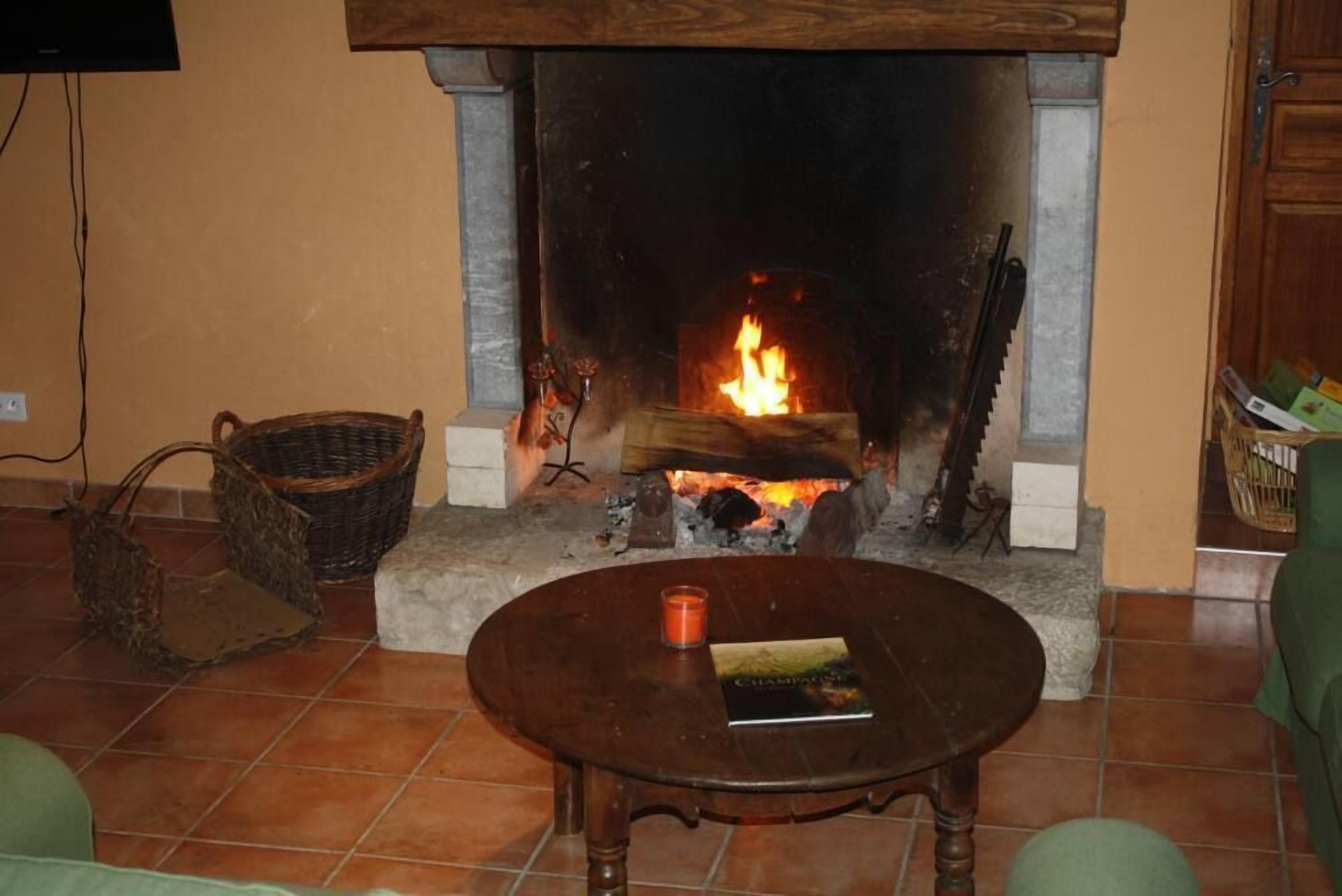 Un salon avec une cheminée, une table ronde en bois sur laquelle sont posés un livre et une bougie, et des paniers en osier sur le sol.