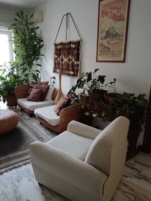 Un salon avec un canapé, un fauteuil, une plante suspendue et un tableau encadré au mur.