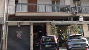 A multi-story building with balconies, a shop at the ground level, and parked cars in front. - Your home in the heart of bari near beach old town and station (Bari)