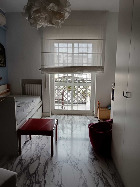 A room with a bed, a table, a chair, a radiator, a window with a view, and a ceiling light fixture.