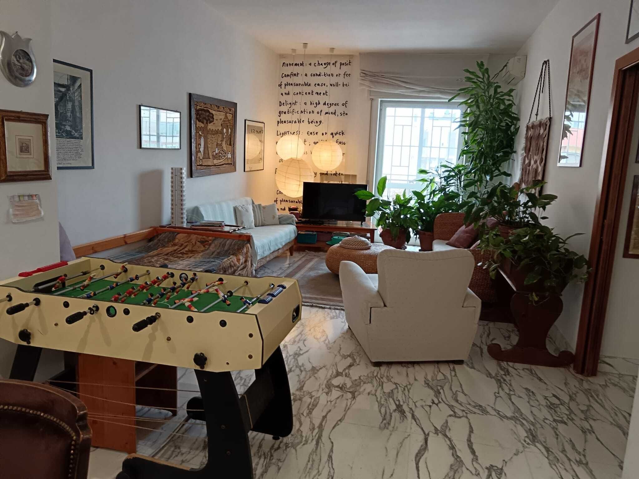 Un salon comprenant une table de baby-foot, un canapé, un téléviseur et un mur orné de texte.