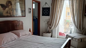 A bedroom with a bed, a wooden headboard, a hanging light fixture, a window with curtains, and a wall-mounted air conditioner. - Your home in the heart of bari near beach old town and station (Bari)