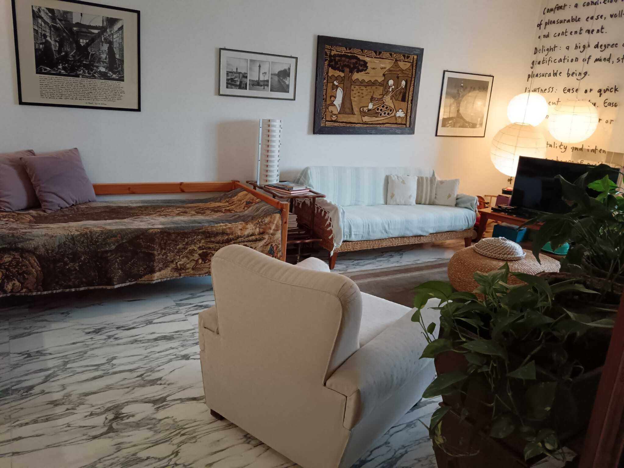 A living room with a sofa, a chair, a TV, and a lamp. There are framed pictures on the wall.
