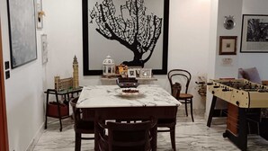 A dining area with a marble table, chairs, a large framed tree artwork, and a foosball table. - Your home in the heart of bari near beach old town and station (Bari)
