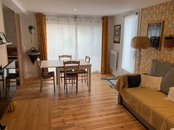 Un salon chaleureux avec un plancher en bois, une table à manger avec des chaises, un canapé et une fenêtre avec des rideaux.