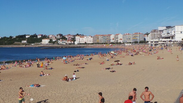 A crowded beach with people sunbathing and swimming.