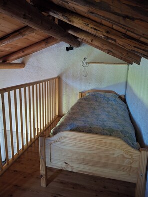 A small, wooden-framed attic bedroom with a sloped ceiling, a single bed, and a wooden railing along one side. - Chalet surrounded by greenery near MTB routes (Castello Tesino)
