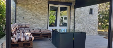 Un espacio de estar al aire libre techado, con pared de piedra, puerta de vidrio y una moderna cocina exterior.