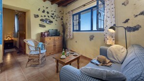 Un salon chaleureux avec un canapé, un fauteuil en osier, une table basse en bois et un téléviseur posé sur un meuble en bois.
